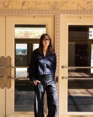 Woman standing in theatre lobby wearing denim top and dark pants