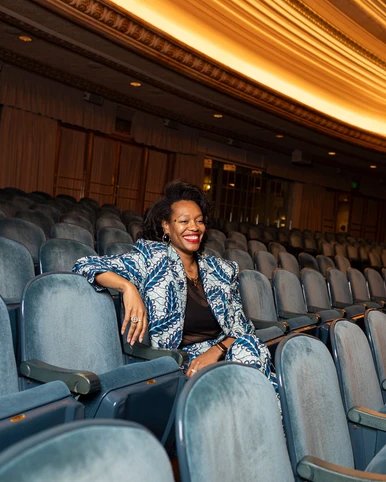 Woman in patterned blue jacket sitting inside theatre