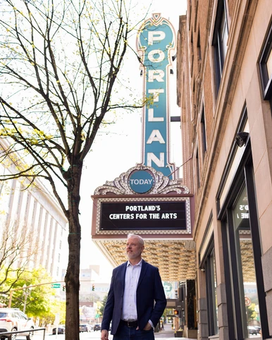 Man in black jacket and white dress shirt standing under Portland sign.