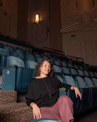Women in black top and mauve pants sitting on stairs next to theatre seats